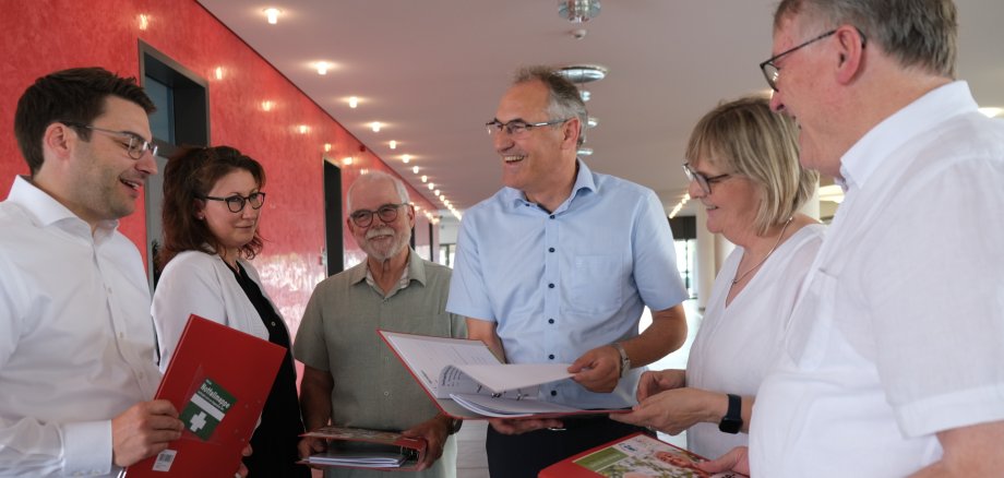 Waren daran beteiligt, dass die neueste Auflage des Vorsorgeordners gedruckt werden kann (von links): Sparkassen-Vorstandsmitglied Benjamin Hirsch, Sonja Bardua vom Referat Demografie der Kreisverwaltung SÜW, Kreisseniorenbeiratsvorsitzender Bernhard Blumenstiel, Landrat Dietmar Seefeldt, Fachkraft Gemeindeschwester plus Ute Wingerter und Kreisseniorenbeiratsmitglied Wolfgang Thiel. Foto: KV SÜW Sechs Personen stehen im Foyer der Sparkasse Südpfalz in Landau und halten Vorsorgeordner in der Hand, während sie miteinander erzählen.