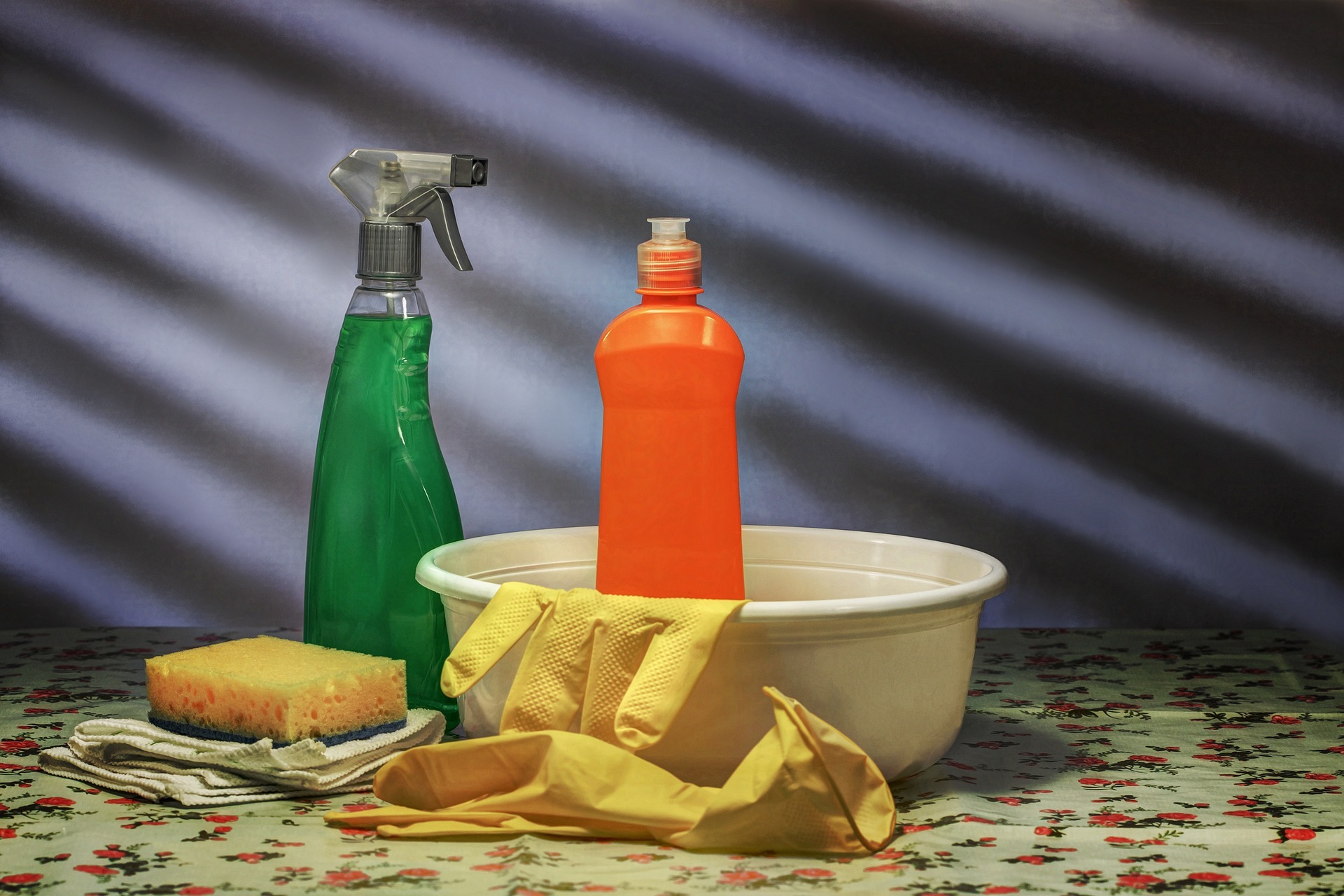Grüne und orangene Sprayflaschen, Waschbecken und Schwamm auf einem Tisch.