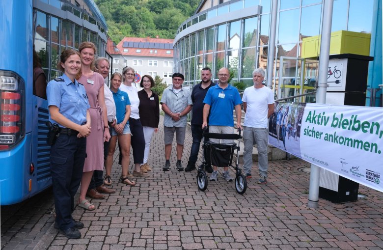 Gemeinsam am Trainingstag: Polizeihauptkommissarin Alexandra Meyer (Polizeiinspektion Landau), Jana Hoyer (Fachkraft GS plus), Werner Kempf (Erster Beigeordneter VG Annweiler am Trifels), Katharina Rösch und Ute Wingerter (Fachkräfte GS plus), Heike Neumann (Leiterin Referat „Demografie“, Landkreis SÜW), Hans-Peter Carius (Seniorenbeauftragter VG Annweiler), Cevin Klein (QNV), Polizeihauptkommissar Steffen Neu (Polizeiinspektion Landau und Verkehrswacht) und Dieter Ehrhardt (Orthopädietechnik Ehrhardt GmbH) (von links nach rechts). Foto: KV SÜW Die Personen stehen zwischen einem blauen Omnibus und dem Eingang zur Verwaltung Annweiler. Am Eingang hängt ein Banner der Verkehrswacht mit der Aufschrift "Aktiv bleiben. Sicher ankommen".