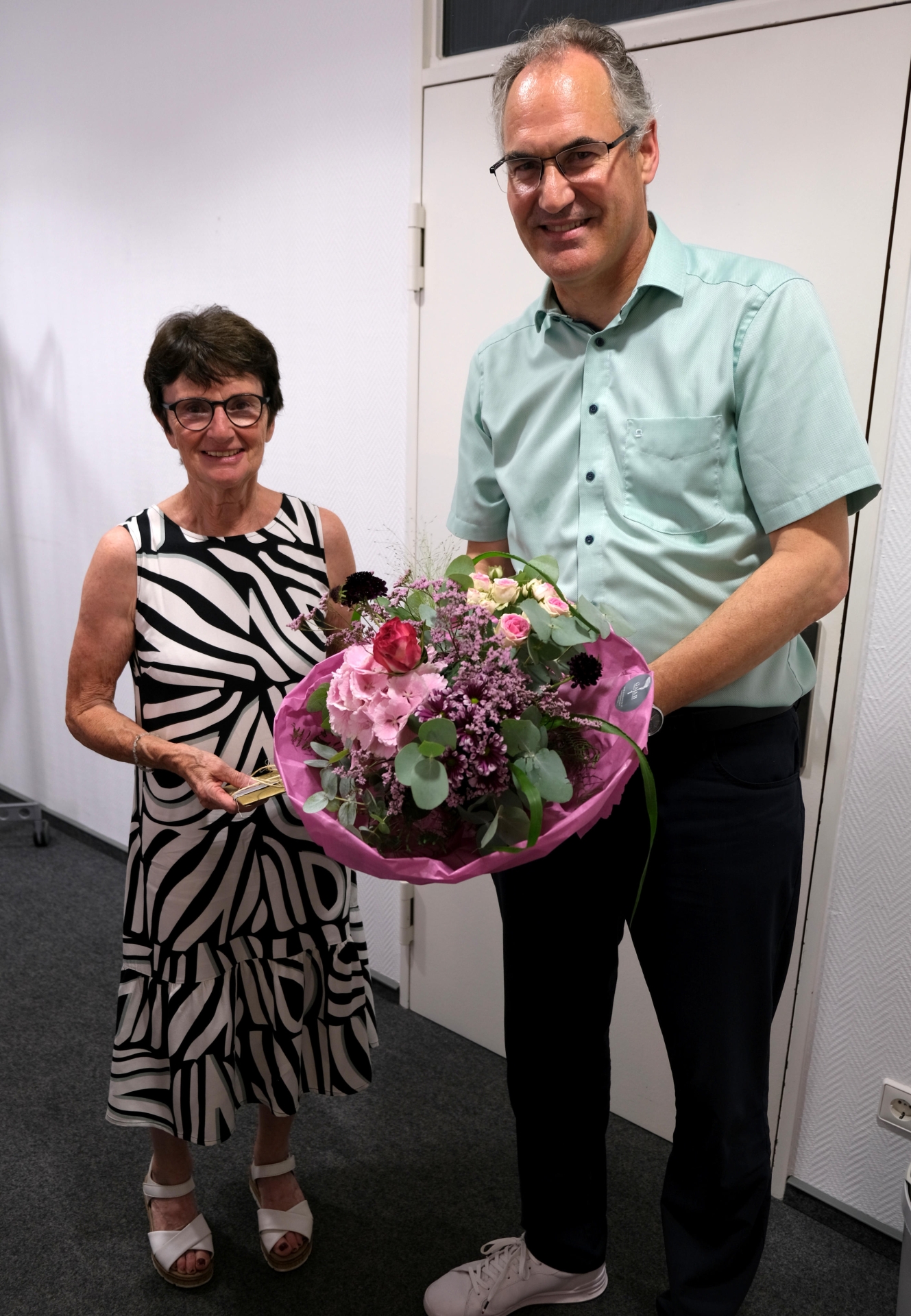 Eine Frau und ein Mann in festlicher Kleidung, er übergibt ihr einen Blumenstrauß.