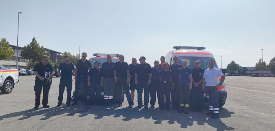 Feuerwehr-Führungskräfte aus der Südpfalz unterstützten beim Waldbrand im Kreis Bad Kreuznach. Foto: KV SÜW/Thiele 15 Personen stehen auf einem betonierten Platz, dahinter Einsatzfahrzeuge.