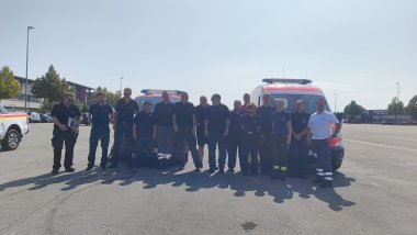 Feuerwehr-Führungskräfte aus der Südpfalz unterstützten beim Waldbrand im Kreis Bad Kreuznach. Foto: KV SÜW/Thiele 15 Personen stehen auf einem betonierten Platz, dahinter Einsatzfahrzeuge.