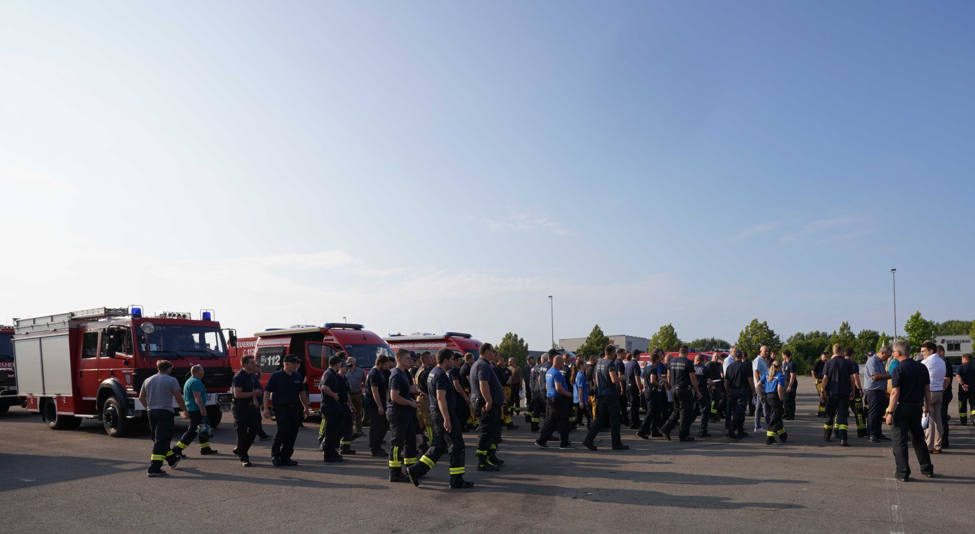 Einsatzkräfte des Brand- und Katastrophenschutzes gehen über den Sammelplatz zu ihren Fahrzeugen. Im Hintergrund stehen mehrere Feuerwehfahrzeuge bereit.