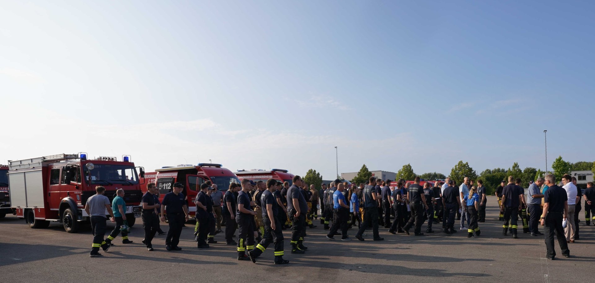 Einsatzkräfte des Brand- und Katastrophenschutzes gehen über den Sammelplatz zu ihren Fahrzeugen. Im Hintergrund stehen mehrere Feuerwehfahrzeuge bereit.