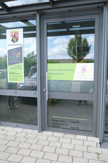 Der Zugang liegt auf der Gebäuderückseite. Foto: KV SÜW Beschriftete Glastür.