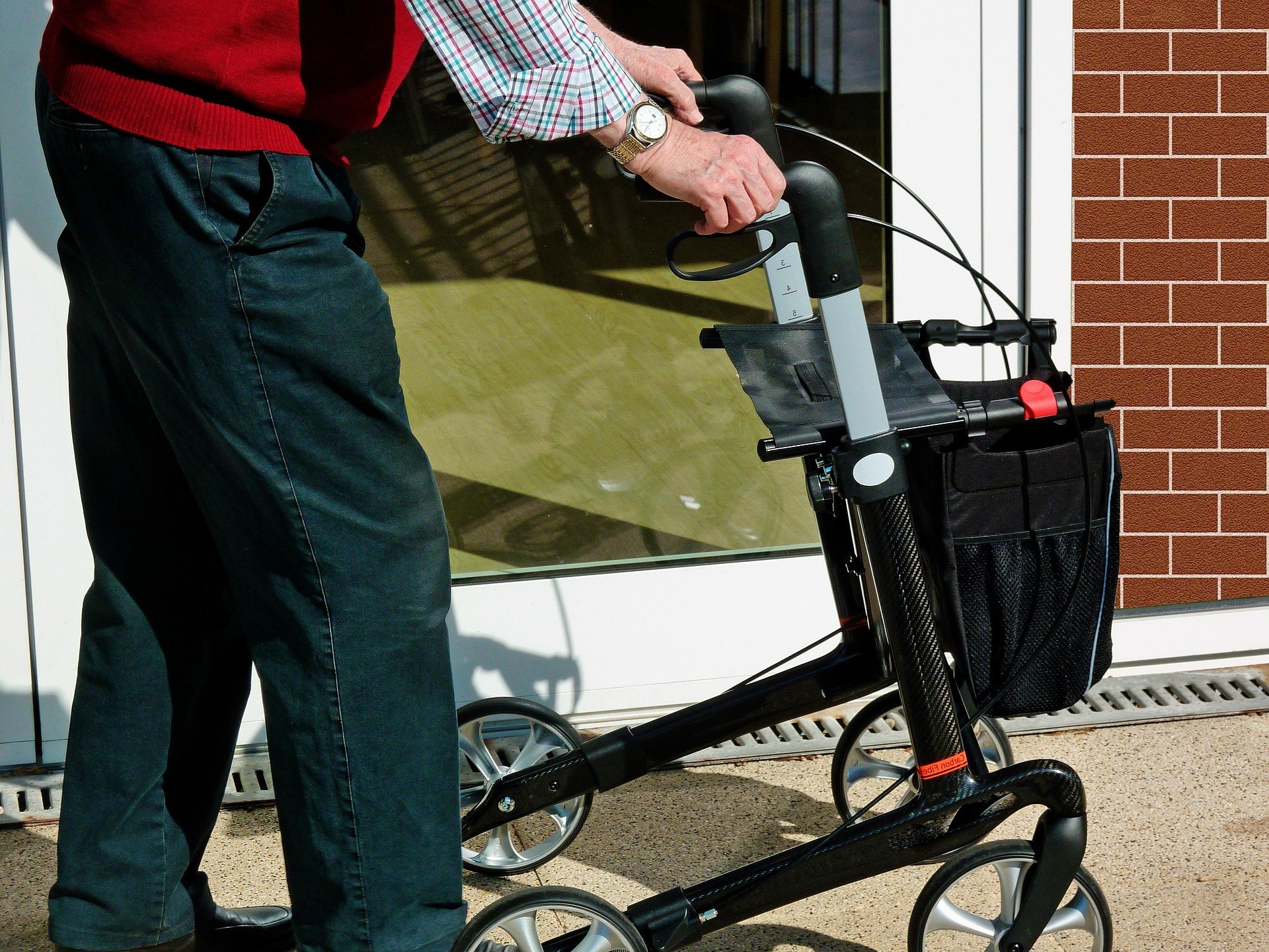 Beine und ein Rollator vor einer Fensterfront.