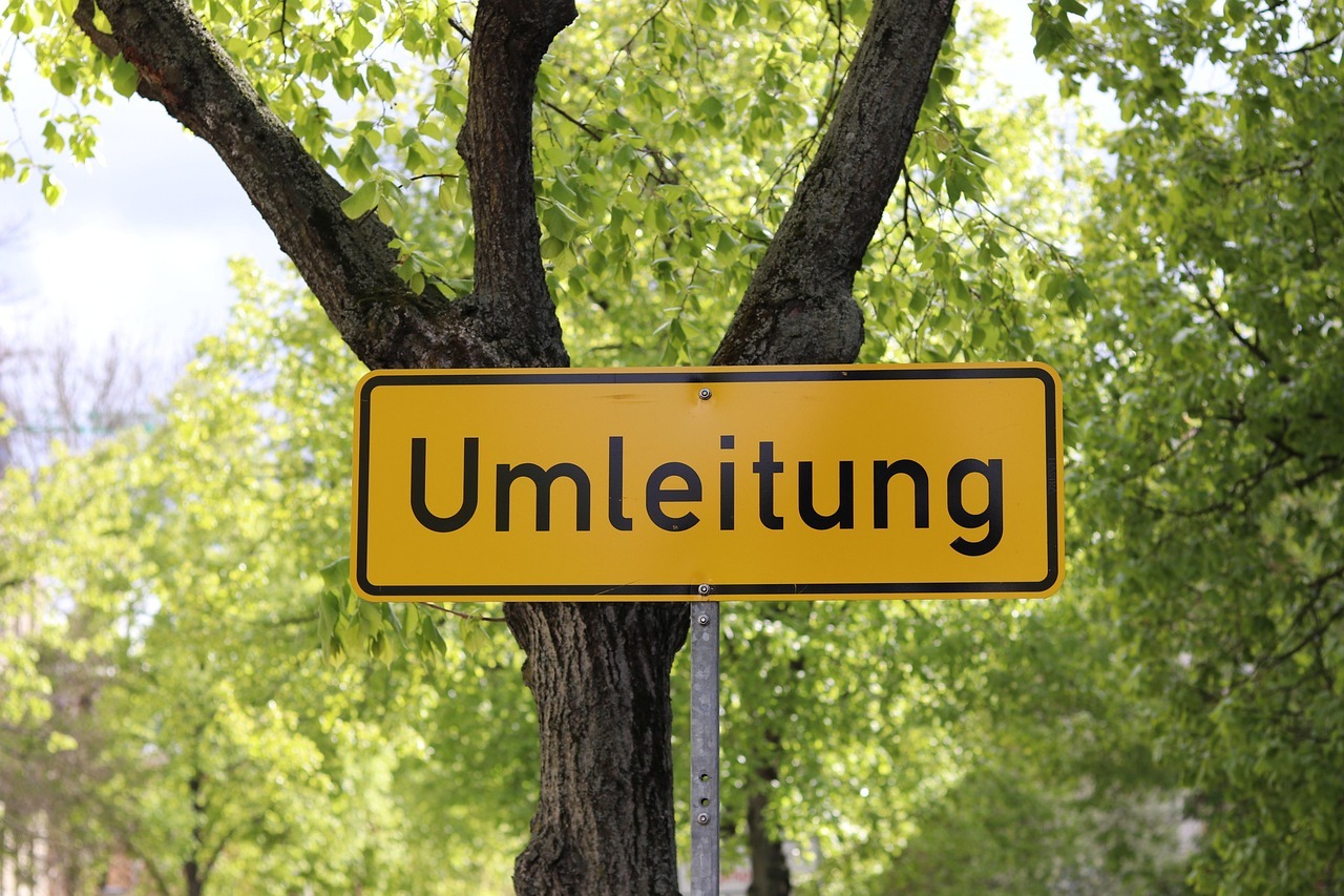 Nahaufnahme eines Umleitungsschilds. Im Hintergrund grüne Laubbäume.