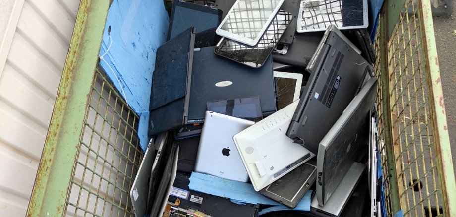 E-Schrott aus dem Landkreis SÜW. Foto: EWW Ein Container ist gefüllt mit ausrangierten elektronischen Geräten wie Laptops, Tablets und Computermonitoren. Die Geräte liegen unsortiert übereinander und sind als Elektroschrott gesammelt.