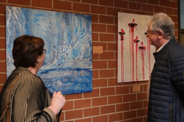 Eine Frau und ein Mann betrachten ein abstraktes Gemälde am einer Ziegelwand.