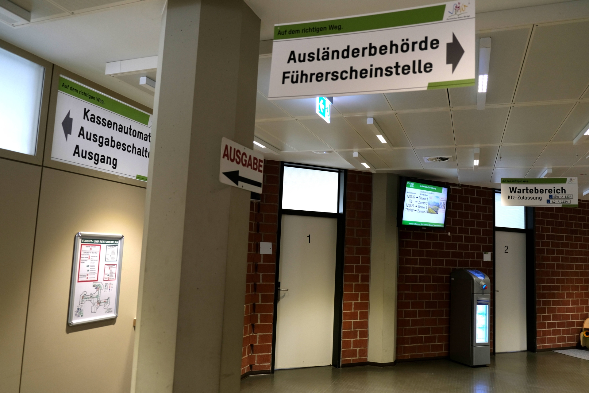 Wartebereich Kfz-Zulassung im Hintergrund, vorn Schild mit Aufschrift "Führerscheinstelle, Ausländerbehörde"