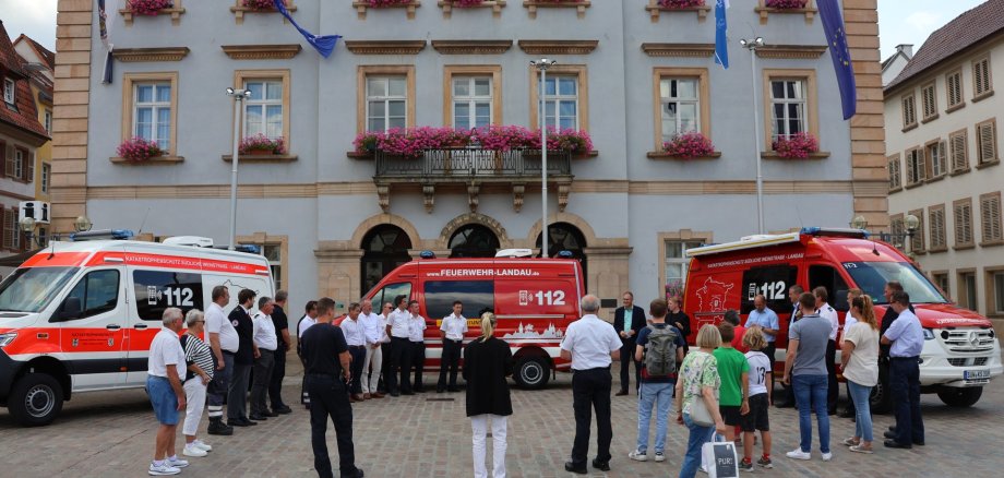 Fahrzeuge und Menschen vor dem Rathaus Landau.