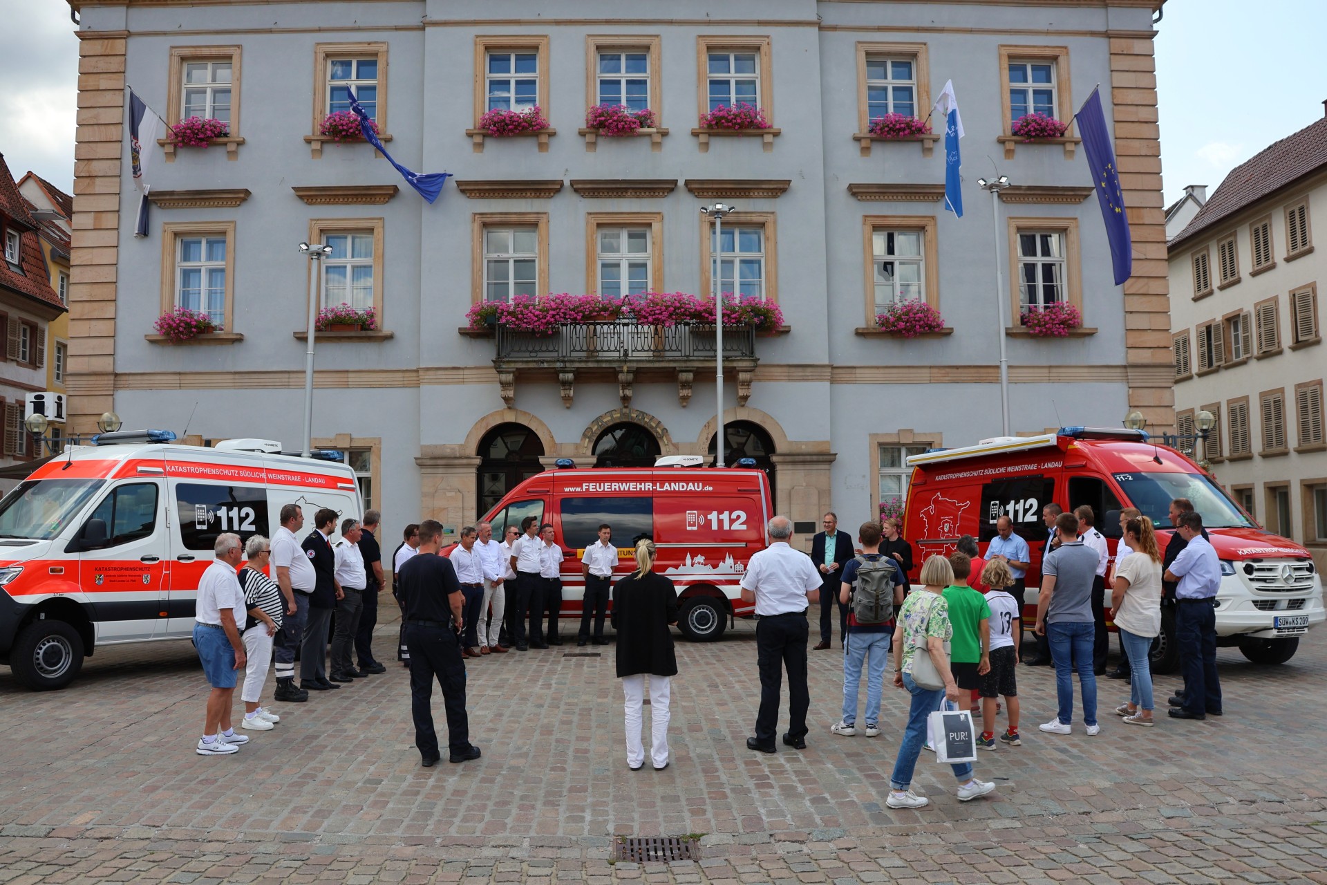 Fahrzeuge und Menschen vor dem Rathaus Landau.