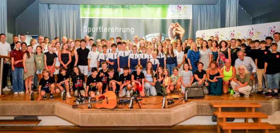 Auf einer Bühne stehen zahlreiche Sportlerinnen und Sportler in schicker Kleidung, die in die Kamera lächeln.