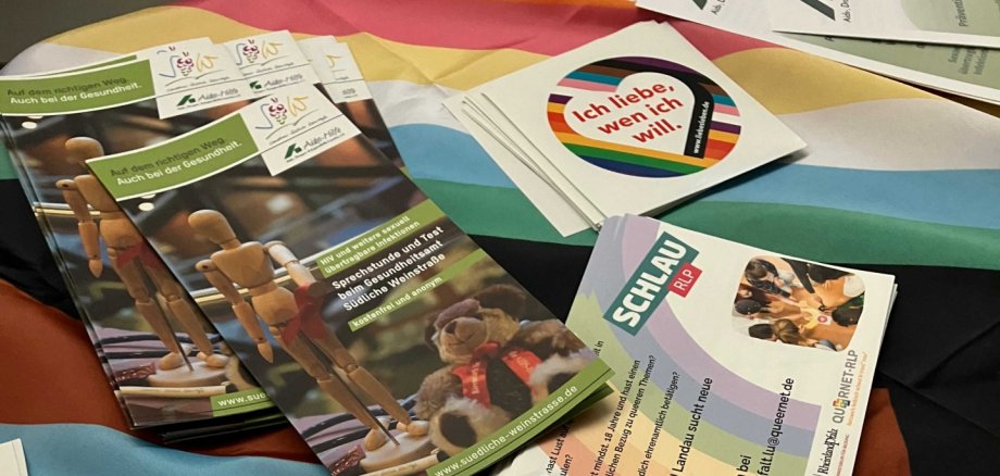 Verpackte Kondome, Flyer und eine Regenbogenfahne liegen auf einem Tisch.