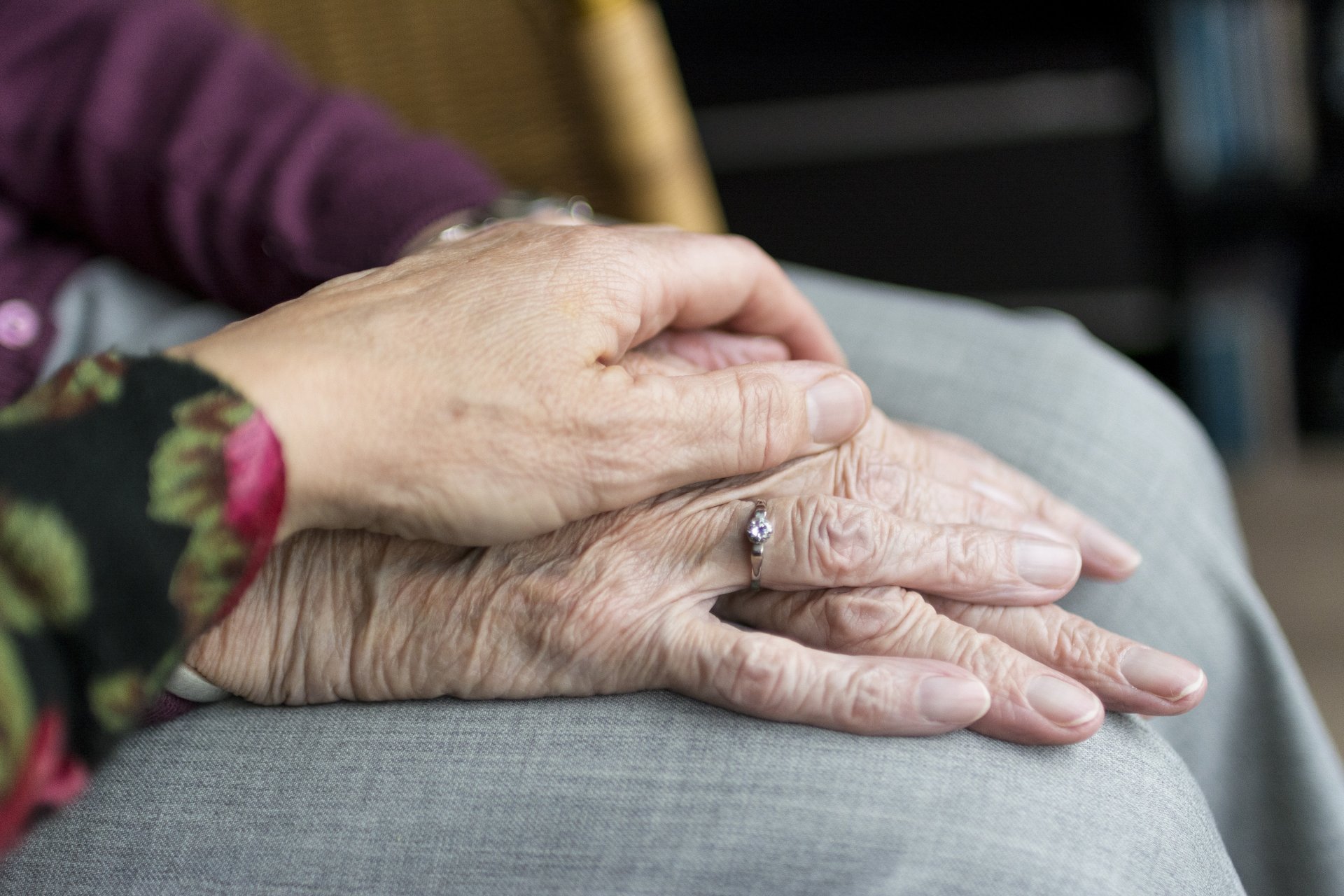 Nahaufnahme zweier übereinanderliegender Hände. Eine jüngere Hand liegt behutsam auf der Hand eines älteren Menschen, der einen Ring trägt.