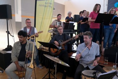 Eine Live-Band aus Musikern der Region und der Kreismusikschule wirkte wieder mit. Foto: KV SÜW Fünf Musiker vor der Bühne, mit Schlagzeug, Gitarre, Bass-Gitarre, Posaune und Akkordeon.
