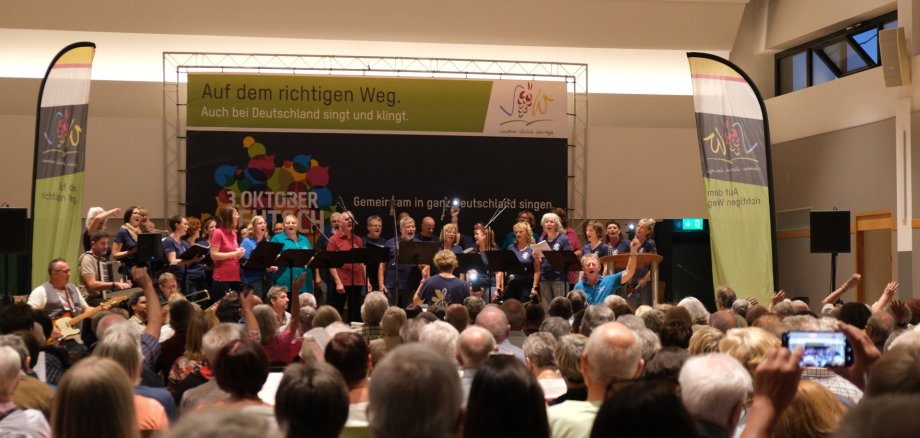 Gesang aus hunderten Kehlen gab es in Insheim zu hören. Foto: KV SÜW Blick über einen voll besetzten Saal zur ebenfalls dicht befüllten Bühne: Chöre, Musiker und Dirigenten im Einsatz.