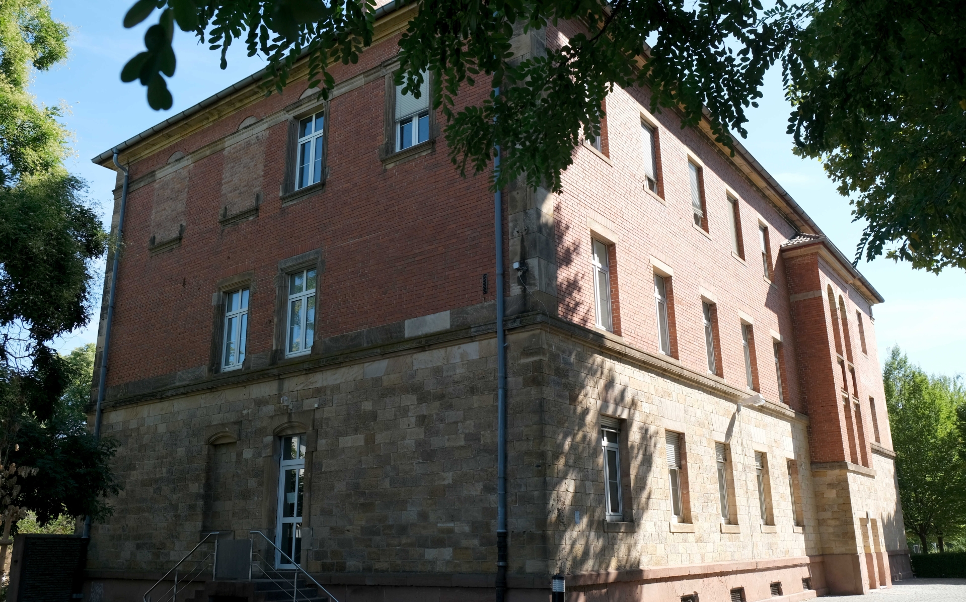 Außenansicht eines dreigeschossigen Gebäudes mit einer Fassade aus roten Backstein und hellem Naturstein im unteren Bereich.