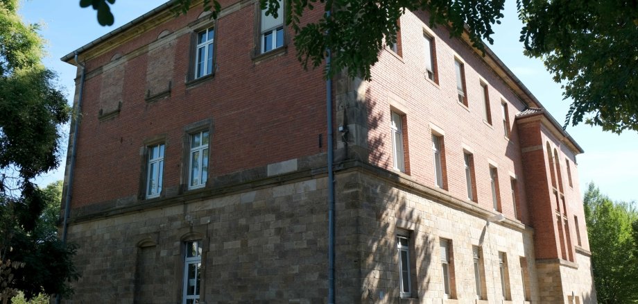 Außenansicht eines dreigeschossigen Gebäudes mit einer Fassade aus roten Backstein und hellem Naturstein im unteren Bereich.