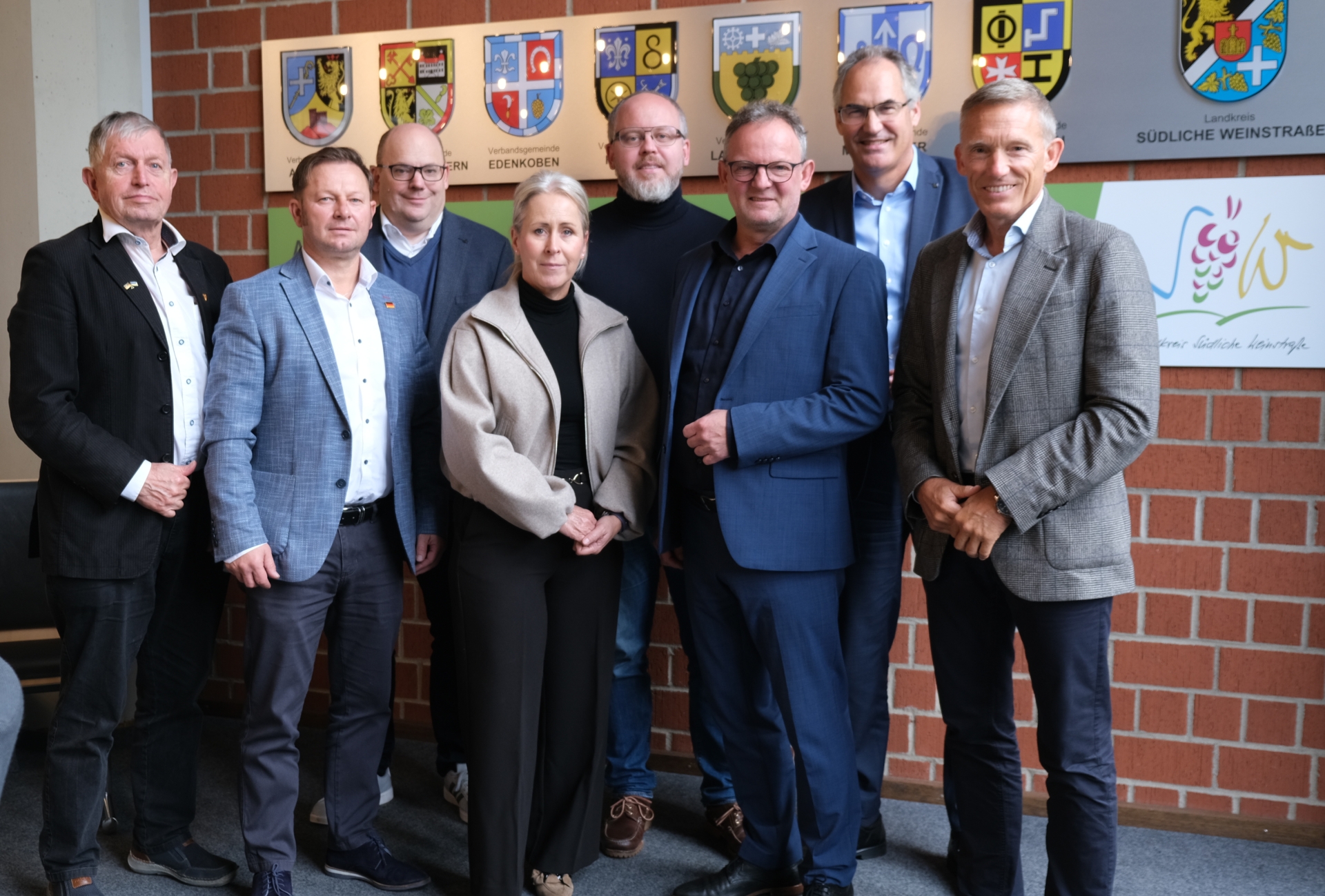 Personen stehen vor einer Wand mit Wappen aus dem Landkreis Südliche Weinstraße.