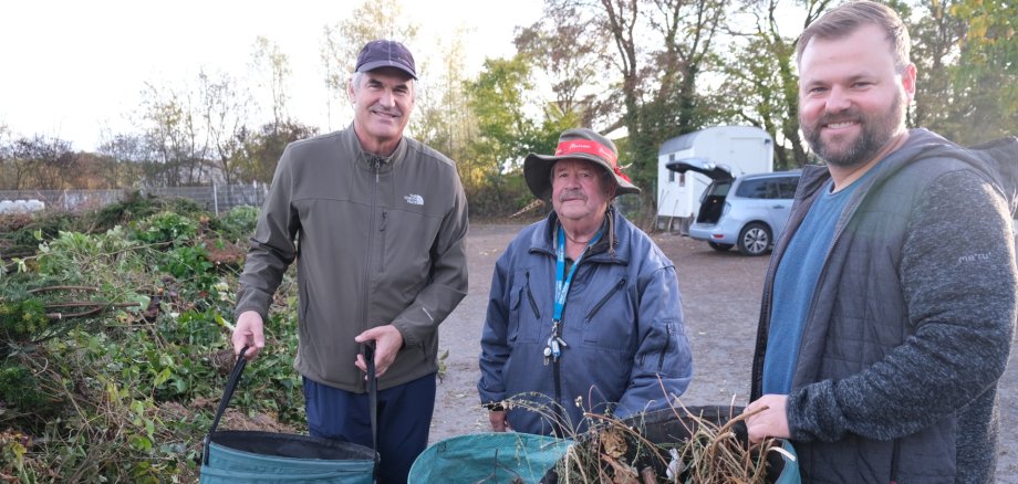 Landrat Dietmar Seefeldt (links), Mitarbeiter Dieter Trapp und Offenbachs Bürgermeister Simon Wingerter (rechts) auf der frisch sanierten Grünschnitt-Annahmestelle. Foto: KV SÜW Drei Männer mit Körben voller Strauchschnitt, im Hintergrund ein Auto mit offenem Kofferraum.