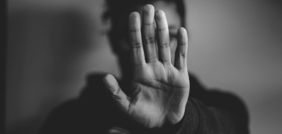 Stopp. Symbolbild: Unsplash Schwarz-weiß-Fotografie einer Person, die ihre Hand mit der Handfläche nach vorne abwehrend vor ihr Gesicht hält.
