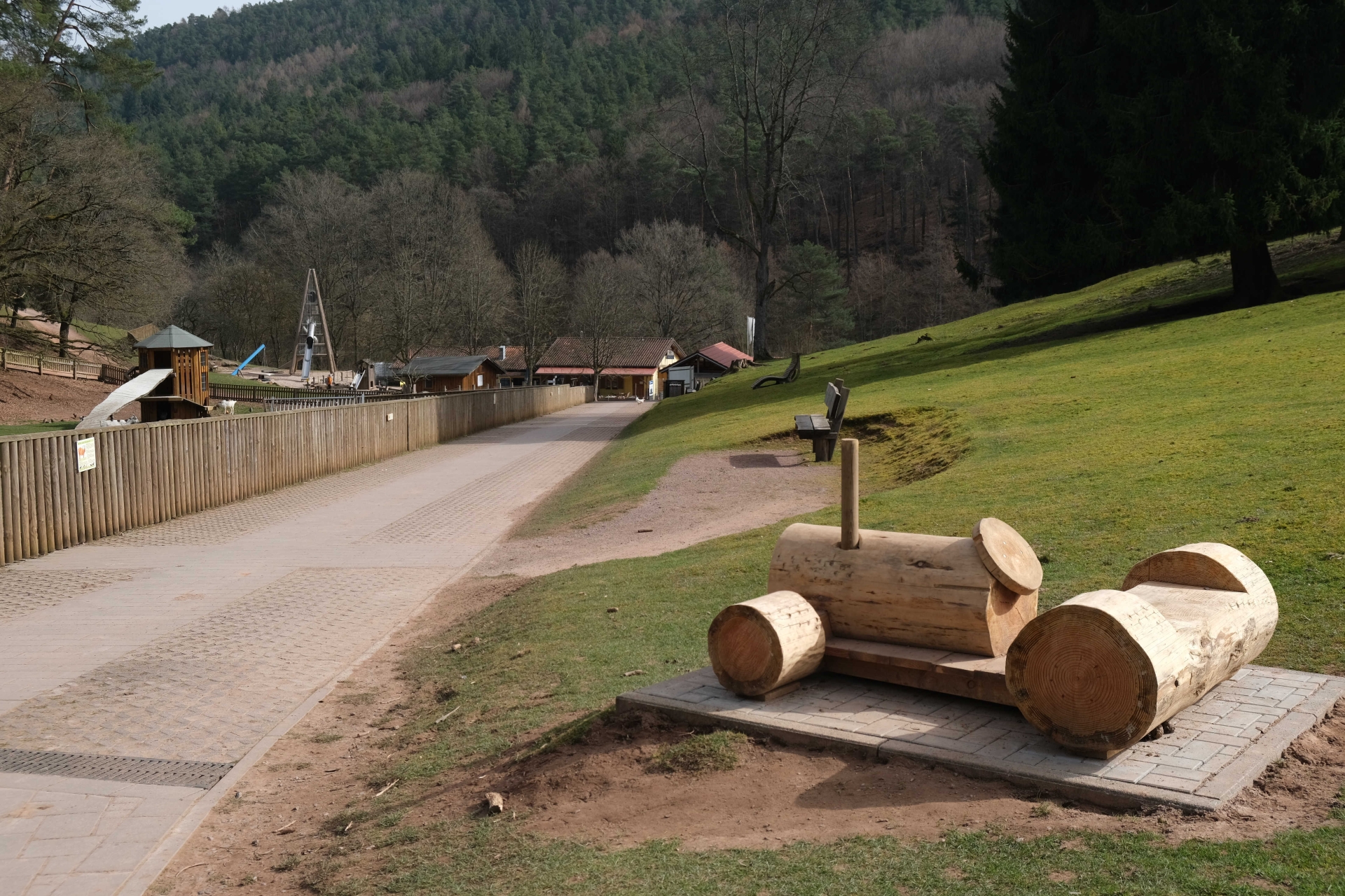 Im Vordergrund ein Traktor aus Holz, im Hintergrund eine Riesenrutsche im Wildpark Silz.