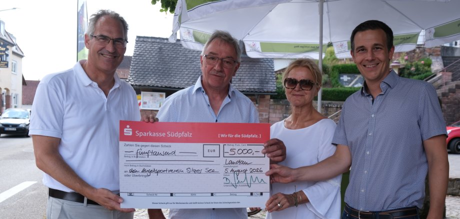 Vier Personen stehen im Freien zusammen und präsentieren einen großen Spendenscheck der Sparkasse Südpfalz über 5.000 Euro.
