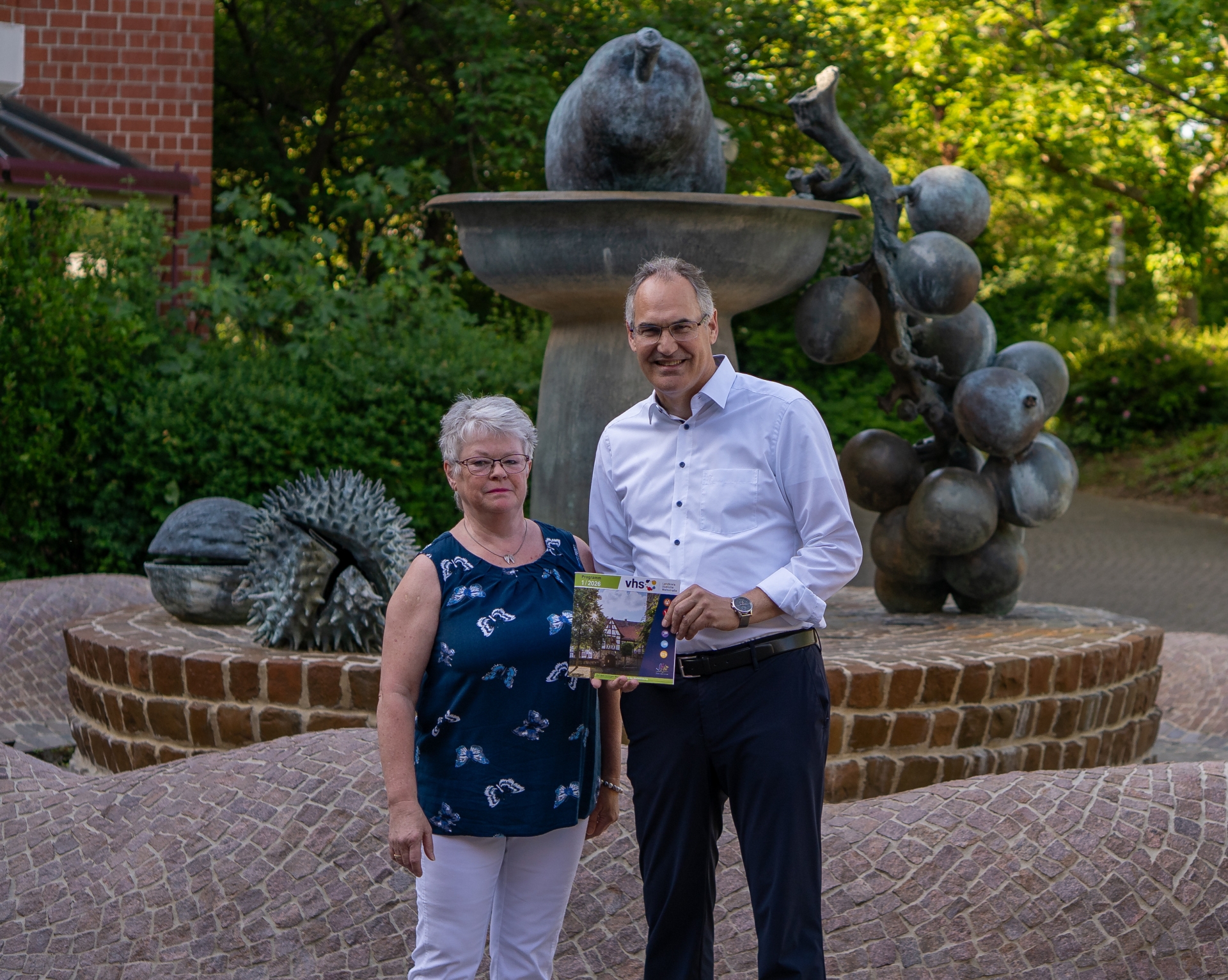 Judith Hammer und Landrat Dietmar Seefeldt stehen gemeinsam am Brunnen vor dem Kreishaus in Landau.