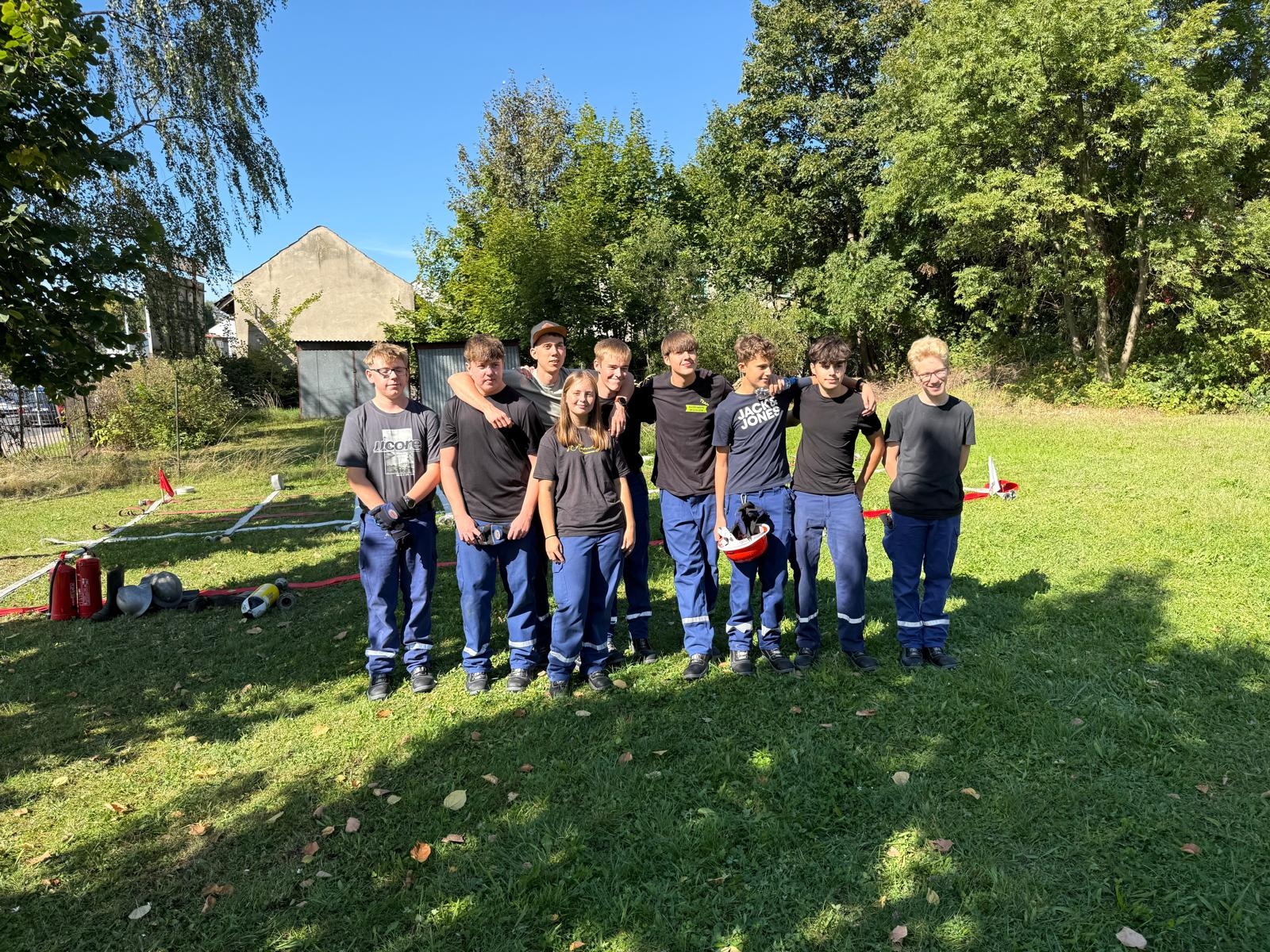 Eine Gruppe Jugendlicher in einheitlicher Einsatzkleidung steht gemeinsam auf einer Wiese und posiert für ein Gruppenfoto.