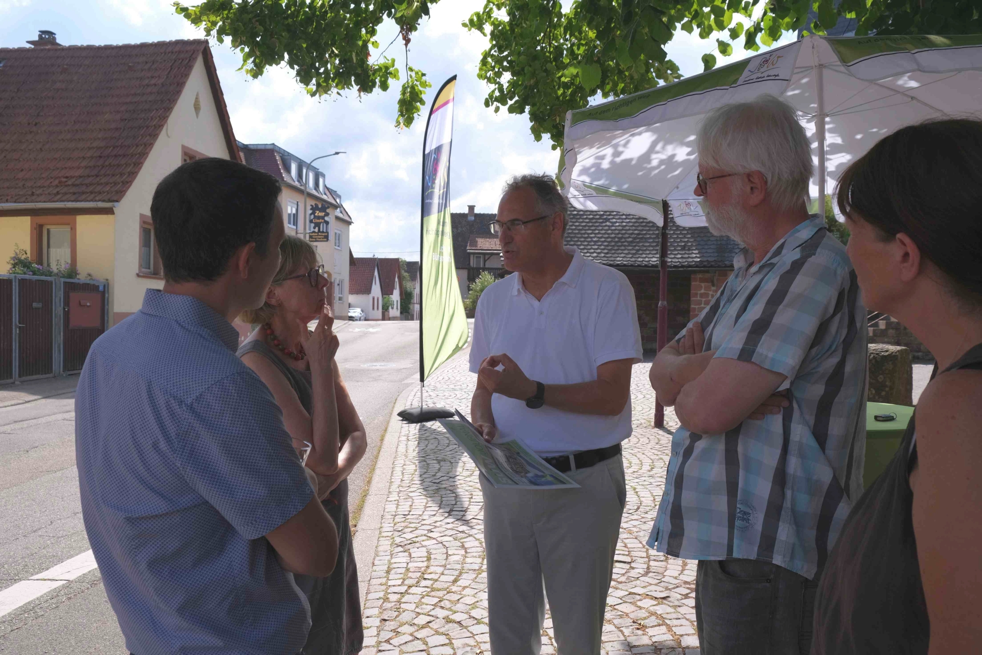 Mehrere Personen stehen an einem Informationsstand im Freien zusammen und unterhalten sich.