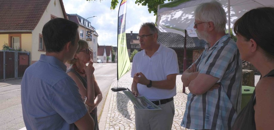 Landrat Dietmar Seefeldt (Mitte) und Bürgermeister Christian Burkhart (links) im Gespräch mit Silzer Bürgerinnen und Bürgern auf dem Lindenplatz. Foto: KV SÜW Mehrere Personen stehen an einem Informationsstand im Freien zusammen und unterhalten sich.