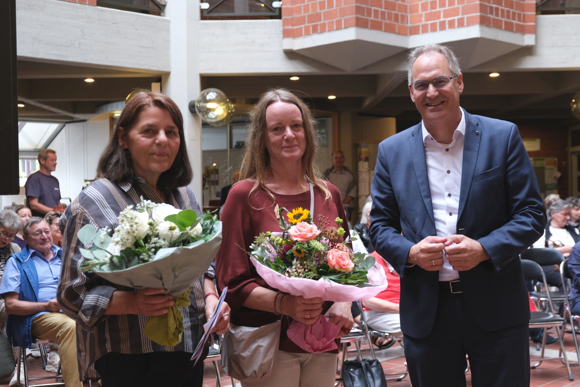 Zwei Frauen mit Blumensträußen stehen gemeinsam mit Landrat Dietmar Seefeldt im Foyer der Kreisverwaltung.
