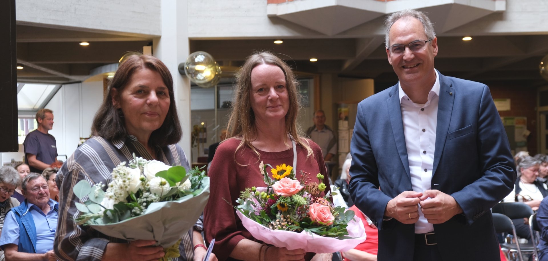 Zwei Frauen mit Blumensträußen stehen gemeinsam mit Landrat Dietmar Seefeldt im Foyer der Kreisverwaltung.