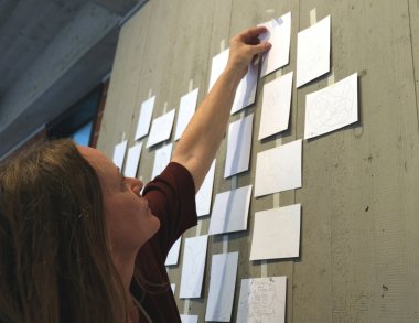 „Gemeinsam eine Linie ziehen im Tempo des Atems“ heißt das Werk, das die Besucherinnen und Besucher der Vernissage im Kreishaus SÜW gemeinsam haben entstehen lassen. Foto: KV SÜW Eine Frau befestigt eine Karte an einer Wand, an der bereits zahlreiche weitere Karten angebracht sind.