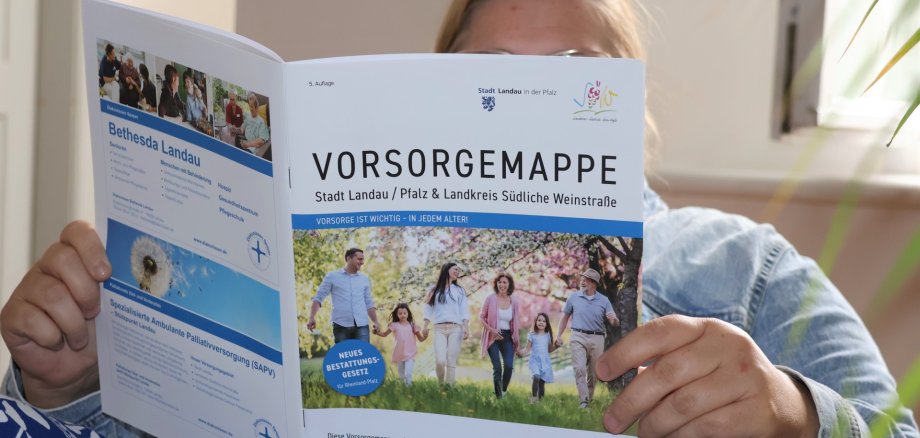 Die fünfte Auflage der Vorsorgemappe ist ab sofort kostenlos beim Bürgerbüro der Stadt Landau im Rathaus, im Kreishaus sowie in den Dienstgebäuden 2 und 3 der Kreisverwaltung Südliche Weinstraße und bei allen Verbandsgemeindeverwaltungen im Landkreis erhältlich. Foto: Stadt Landau Eine Person hält eine aufgeklappte Vorsorgemappe der Stadt Landau und Landkreises Südliche Weinstraße in die Kamera.
