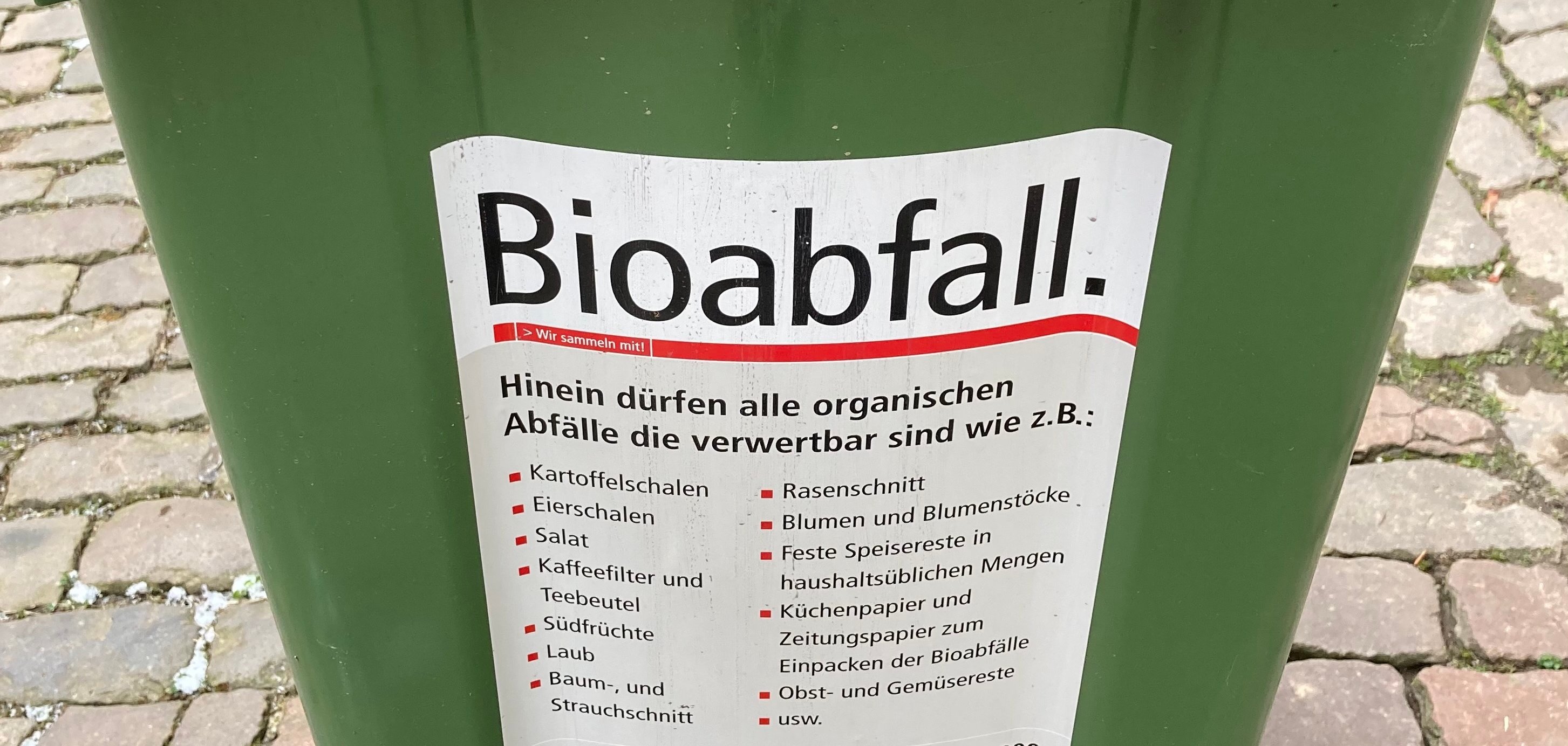 Nahaufnahme einer Biomülltonne. Ein Aufkleber listet die Abfallarten auf, die in der Tonne entsorgt werden dürfen. 