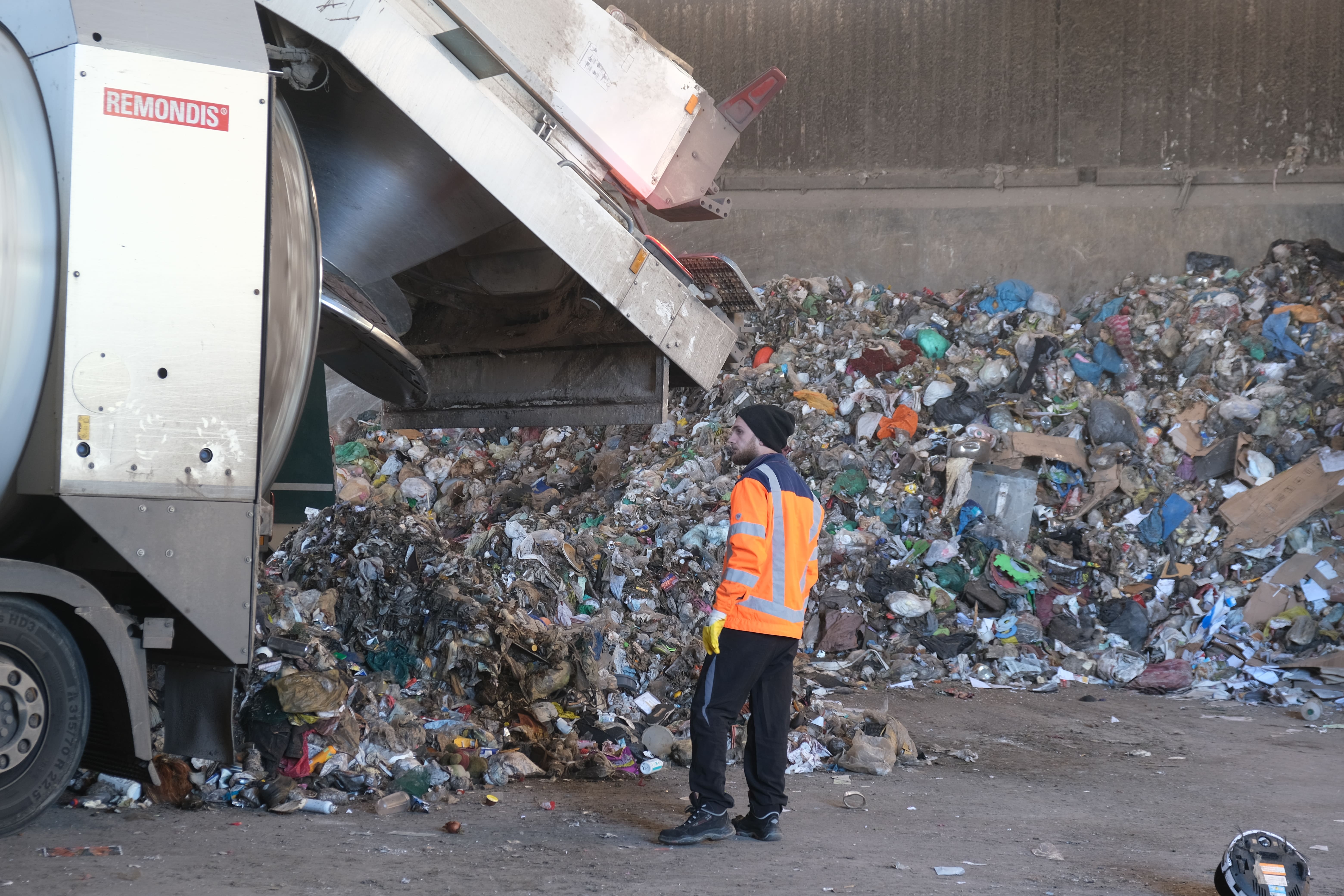Ein Müllwerker steht neben einem Fahrzeug mit geöffneter Klappe. 