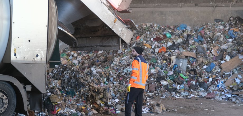 Ein Müllwerker steht neben einem Fahrzeug mit geöffneter Klappe. 