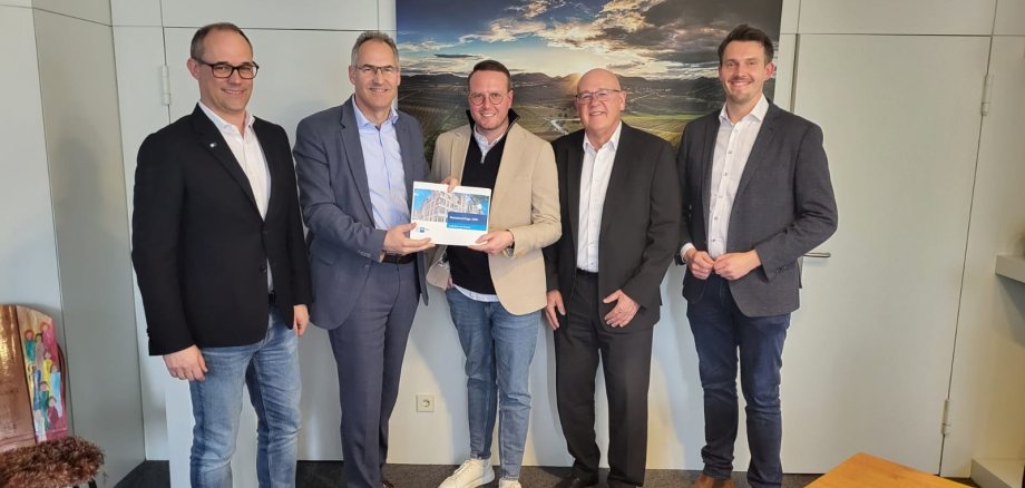 Gruppenbild: Marco Feig, Dietmar Seefeldt, Dominik Uhl, Uwe König und Tim Wiedemann (von links nach rechts) stehen nebeneinander in einem Büroraum.  Hinter ihnen hängt ein Landschaftsfoto an der Wand, dass Weinberge am Rand des Pfälzerwalds zeigt.