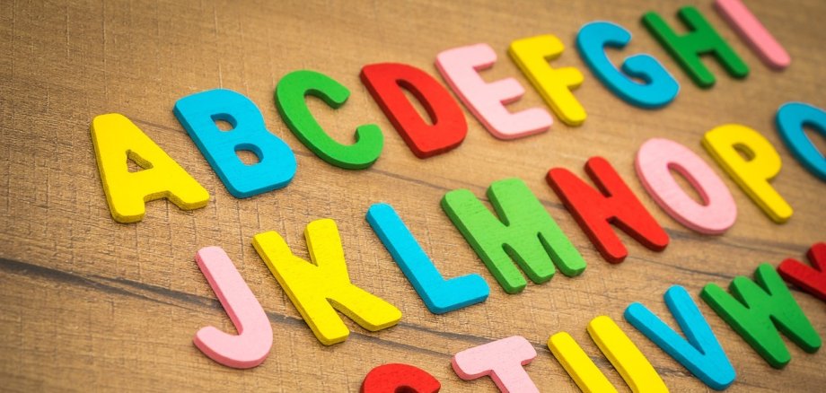 Bunte Buchstaben aus Plastik liegen in alphabetischer Reihenfolge auf einem Tisch.