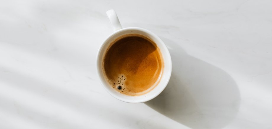 Eine Tasse mit Kaffee, von oben fotografiert. Auf weißem Boden. Foto: yousafbhutta via Pixaby