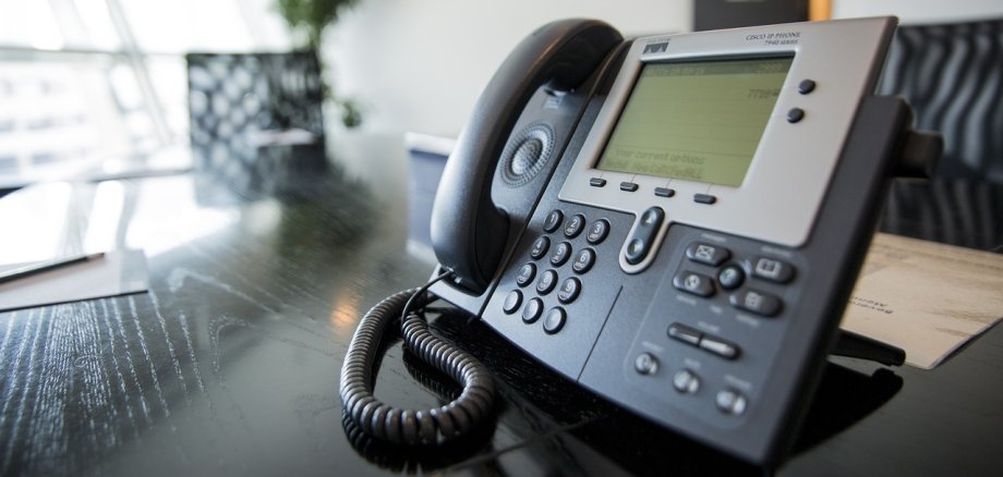 Ein Telefon im Büro. Foto: Pixabay Nahaufnahme eines Cisco IP-Telefons auf einem Konferenztisch in einem modernen, hellen Besprechungsraum. Der Telefonhörer liegt auf der Basis, das Display zeigt eine Liste von Optionen. Im Hintergrund ist eine Zimmerpflanze sowie ein Teil des Konferenzraums zu sehen (generiert mit Hilfe von KI)