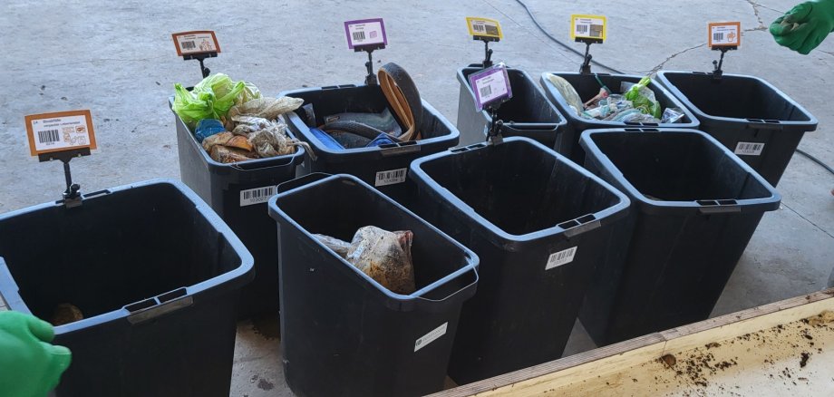 Mehrere schwarze Mülleimer stehen zur systematischen Trennung des Restmülls in seine verschiedenen Bestandteile bereit.