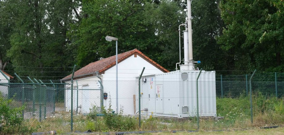 Neben einem kleinen Häuschen steht ein Container mit einem Schornstein, in dem die Technik der Schwachgasanlage untergebracht ist. 
