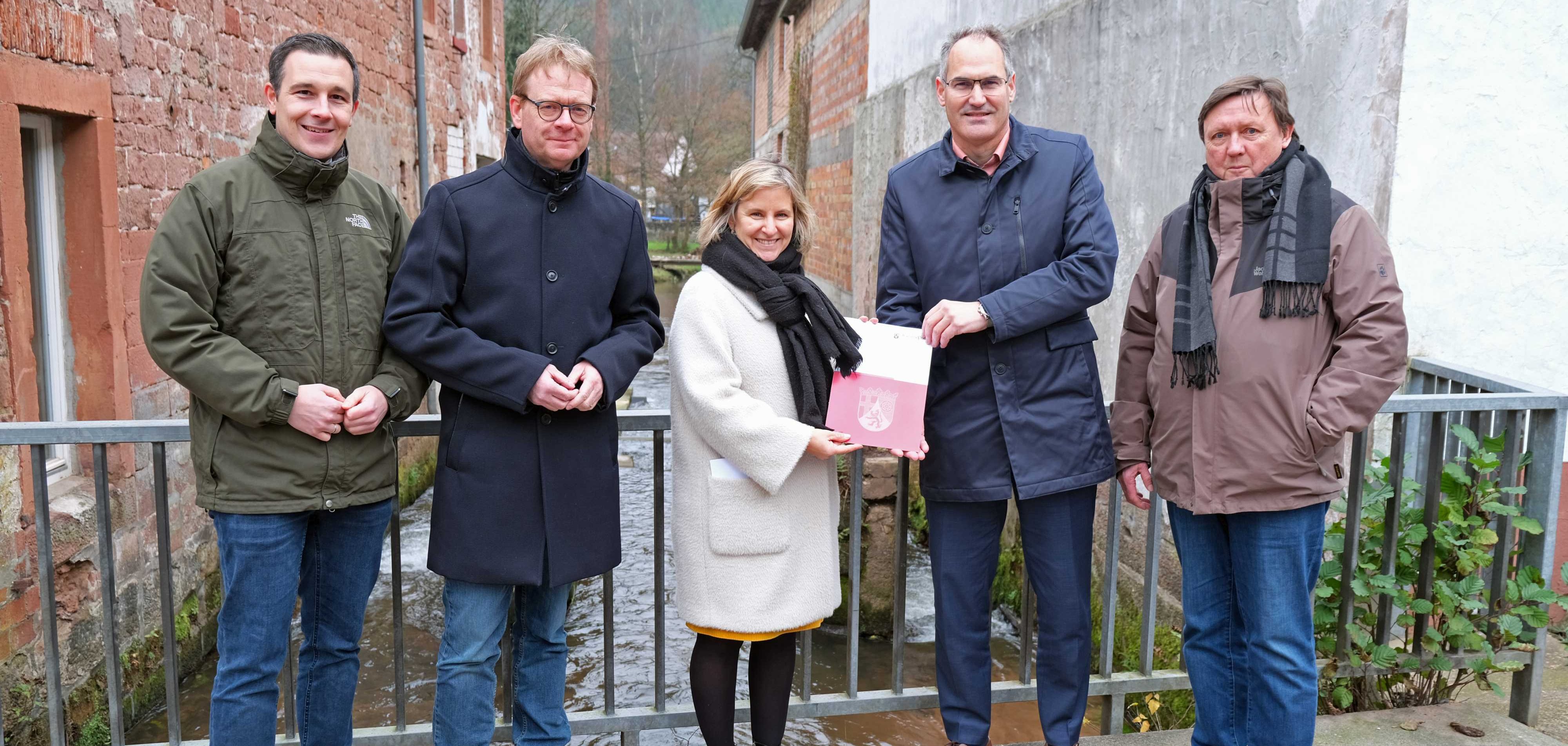Umwelt- und Klimaschutzministerin Katrin Eder überreicht Landrat Dietmar Seefeldt den Förderbescheid für den neuen Fischpass, eine Duchgängigkeitsmaßnahme an der Queich in Rinnthal. Mit im Bild Christian Burkhart, Bürgermeister der Verbandsgemeinde Annweiler am Trifels (links), rechts daneben Bundestagsabgeordneter Dr. Thomas Gebhart und Kreisbeigeordneter Ulrich Teichmann (rechts). Foto: KV SÜW Umwelt- und Klimaschutzministerin Katrin Eder überreicht Landrat Dietmar Seefeldt den Förderbescheid für den neuen Fischpass, eine Duchgängigkeitsmaßnahme an der Queich in Rinnthal. Mit im Bild Christian Burkhart, Bürgermeister der Verbandsgemeinde Annweiler am Trifels, Bundestagsabgeordneter Dr. Thomas Gebhart und Kreisbeigeordneter Ulrich Teichmann auf einer Brücke über der Queich, im Hintergrund der neue Fischpass.