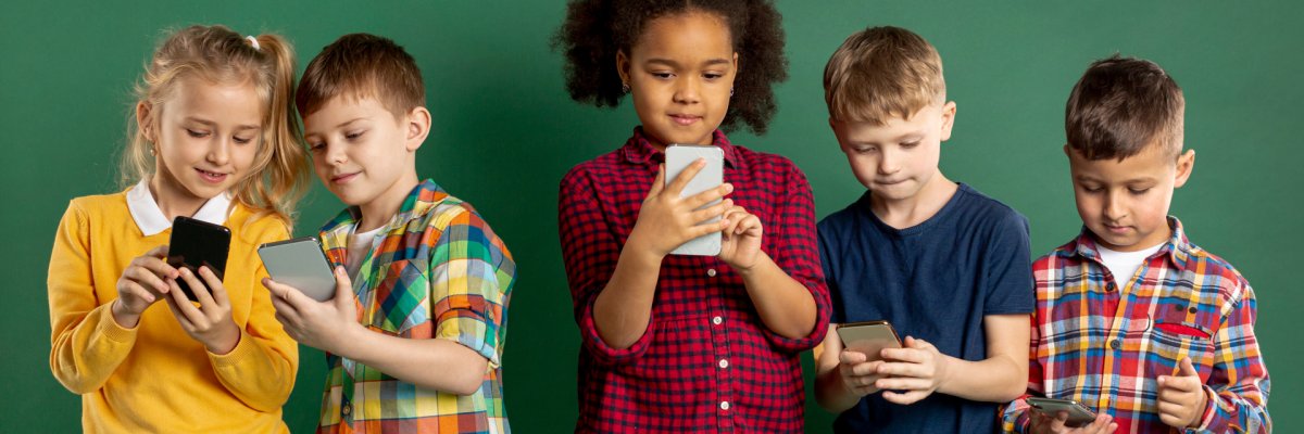 Fünft Kinder stehen nebeneinander vor einem neutralen grünen Hintergrund und schauen jeweils auf ein Smartphone, das sie in Händen halten. Links zeigen sich ein Mädchen und ein Junge gegenseitig etwas auf dem Bildschirm ihres Smarphones.