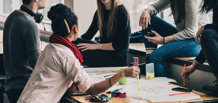 Während der Zeit einer schulischen Aus- oder Fortbildung kann finanzielle Unterstützung durch Schüler- oder Aufstiegs-BAföG beantragt werden. Foto: Pixabay Eine Gruppe junger Menschen sitzt gemeinsam an einem Tisch in einem modernen Raum mit großen Fenstern. Sie arbeiten kreativ an einem Projekt, nutzen bunte Stifte und diskutieren miteinander. Einige sitzen auf der Fensterbank, während eine Person aktiv Notizen auf einem großen Papier macht.