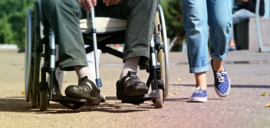 Die Abteilung Soziales unterstützt in verschiedenen Lebenslagen. Foto: Pixabay Junge Frau läuft neben einem Rollstuhlfahrer.