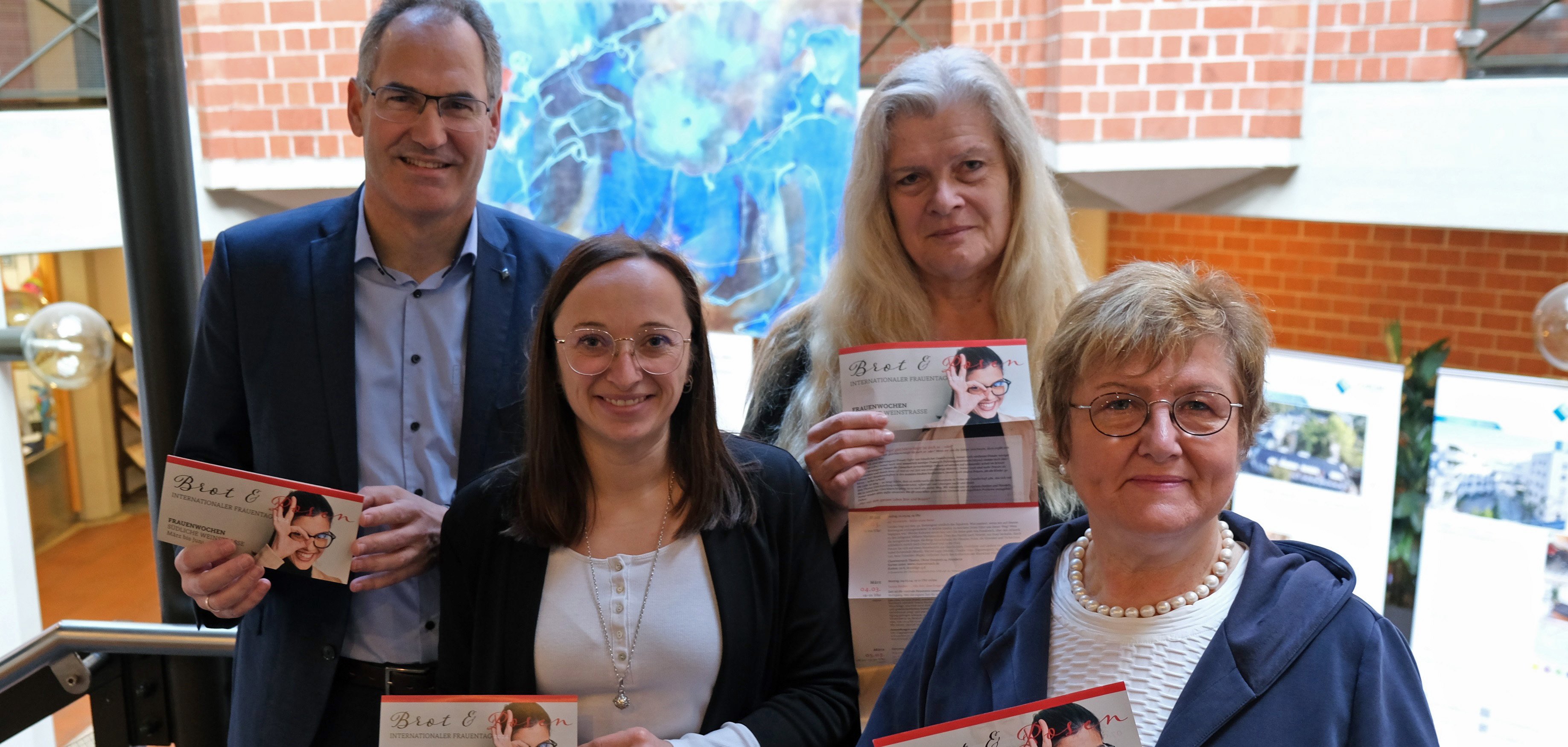 Drei Gleichstellungsbeauftragte im Landkreis Südliche Weinstraße und Landrat Dietmar Seefeldt halten das Programm der Frauenwochen Brot und Rosen 2024 in die Kamera.